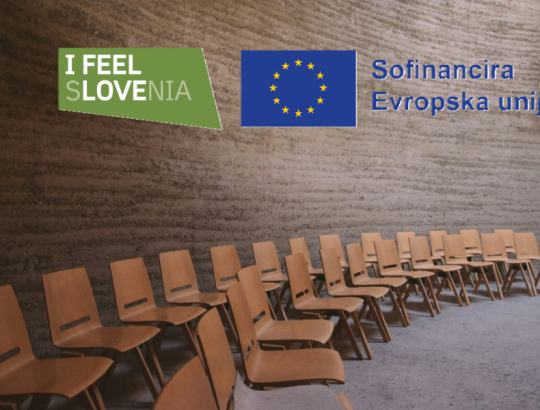 konferenčna dvorana s praznimi lesenimi stoli za udeležence z logotipoma I FEEL SLOVENIA in Sofinancira Evropska unija.